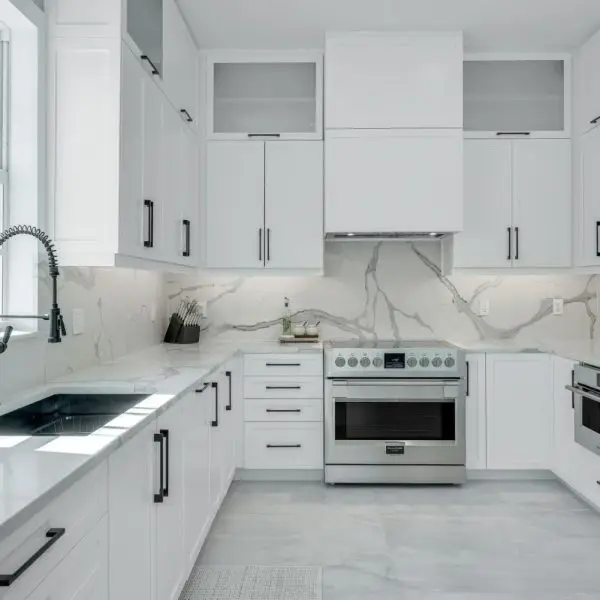Luxury white kitchen with marble backsplash, stainless steel appliances, quartz countertops, and black matte cabinet handles.