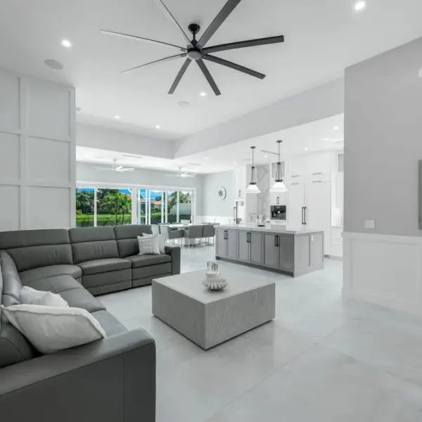 Remodeled living space with gray sectional, quartz island, large windows, custom wall paneling, and sleek ceiling fan.